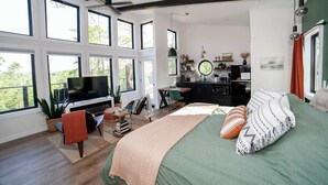 Um quarto espaçoso com uma cama grande, televisão e uma kitchenette ao fundo.