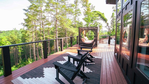 Um deck de madeira com mobiliário externo, com vista para uma área arborizada.