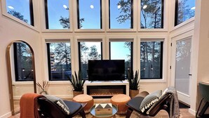 Uma sala de estar moderna com lareira, janelas amplas e uma televisão de tela plana.