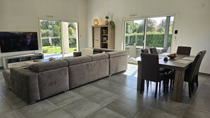 A modern living room with a large sectional sofa, a dining table with chairs, a flat-screen TV, and a sliding glass door leading to a garden. - Villa with swimming pool for 6 people - Air conditioning, Wi-Fi, beach within walking distance (SOLARO)