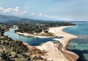 Paisagem costeira com rio, praia e área arborizada.