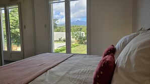 A bedroom with a bed, a view of greenery and mountains through large windows. - Villa with swimming pool for 6 people - Air conditioning, Wi-Fi, beach within walking distance (SOLARO)