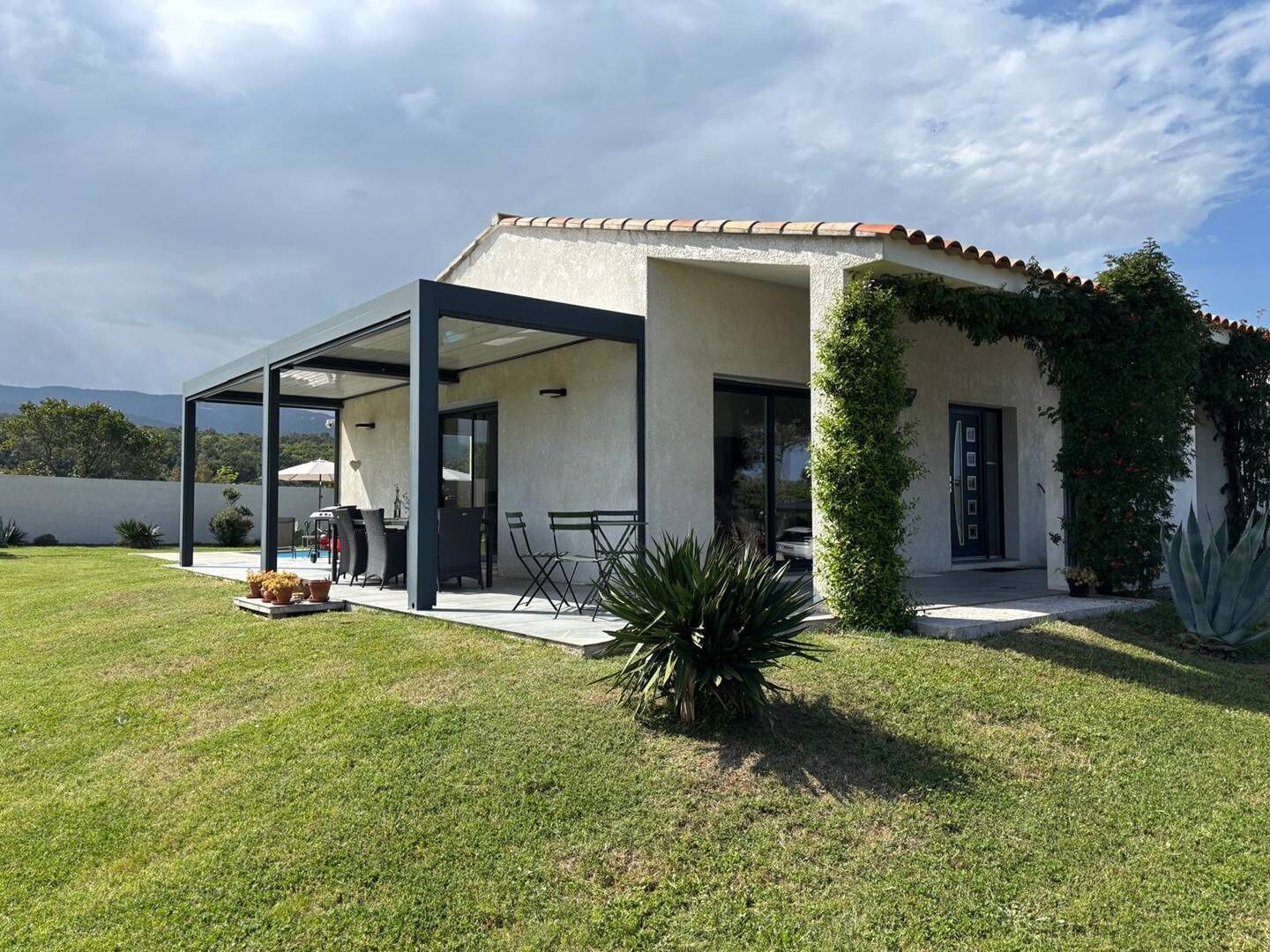 A modern house with a covered patio, a swimming pool, and a well-maintained lawn.