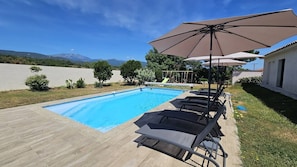 Ein Swimmingpool mit Liegestühlen und Sonnenschirmen, umgeben von einer Holzterrasse und einer Rasenfläche.