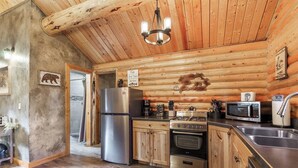 A rustic cabin-style kitchen with wooden walls, a stainless steel refrigerator, a gas stove, and a microwave. - The Bear`s Burrow | 7 Mi to YNP | Private Pond (West Yellowstone)