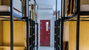 A corridor with bunk beds on either side, leading to a red door with a white sign. - SHARE Hostel & Coffee (Hue)