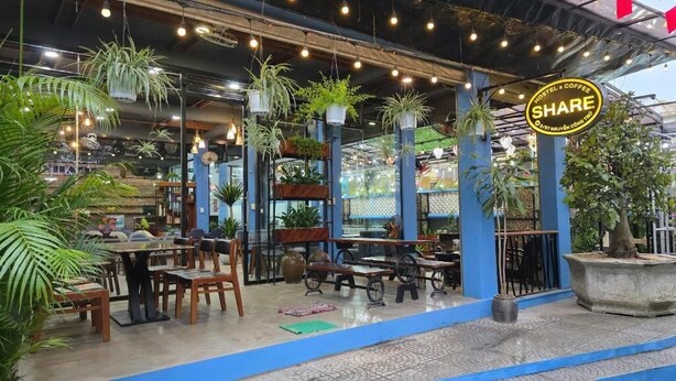 An outdoor cafe area with tables and chairs, surrounded by potted plants and hanging lights. - SHARE Hostel & Coffee (Hue)