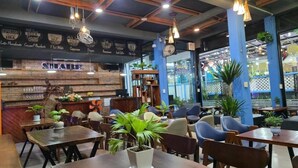 A cozy cafe with wooden tables and chairs, a coffee bar, and various plants. - SHARE Hostel & Coffee (Hue)