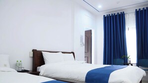 A hotel room with two beds, a nightstand, a window with blue curtains, and a small table with a plant. - SHARE Hostel & Coffee (Hue)