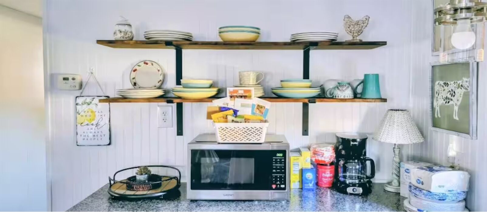 Une cuisine avec des étagères où sont rangées des assiettes et des bols, un four à micro-ondes, une machine à café et un calendrier.