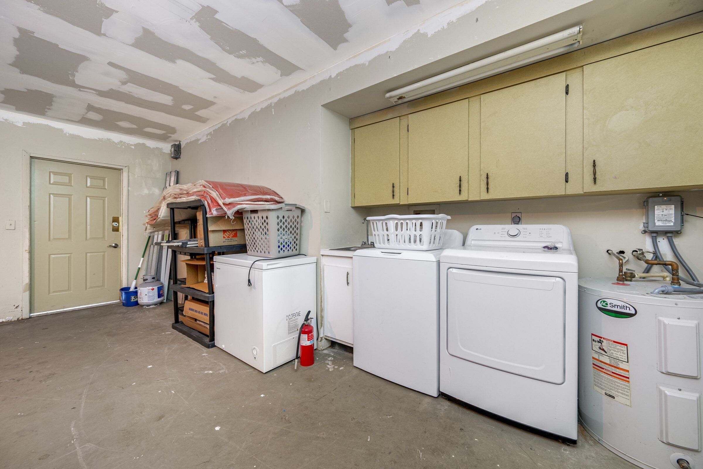 A laundry room with two washing machines, a dryer, and a utility cabinet.