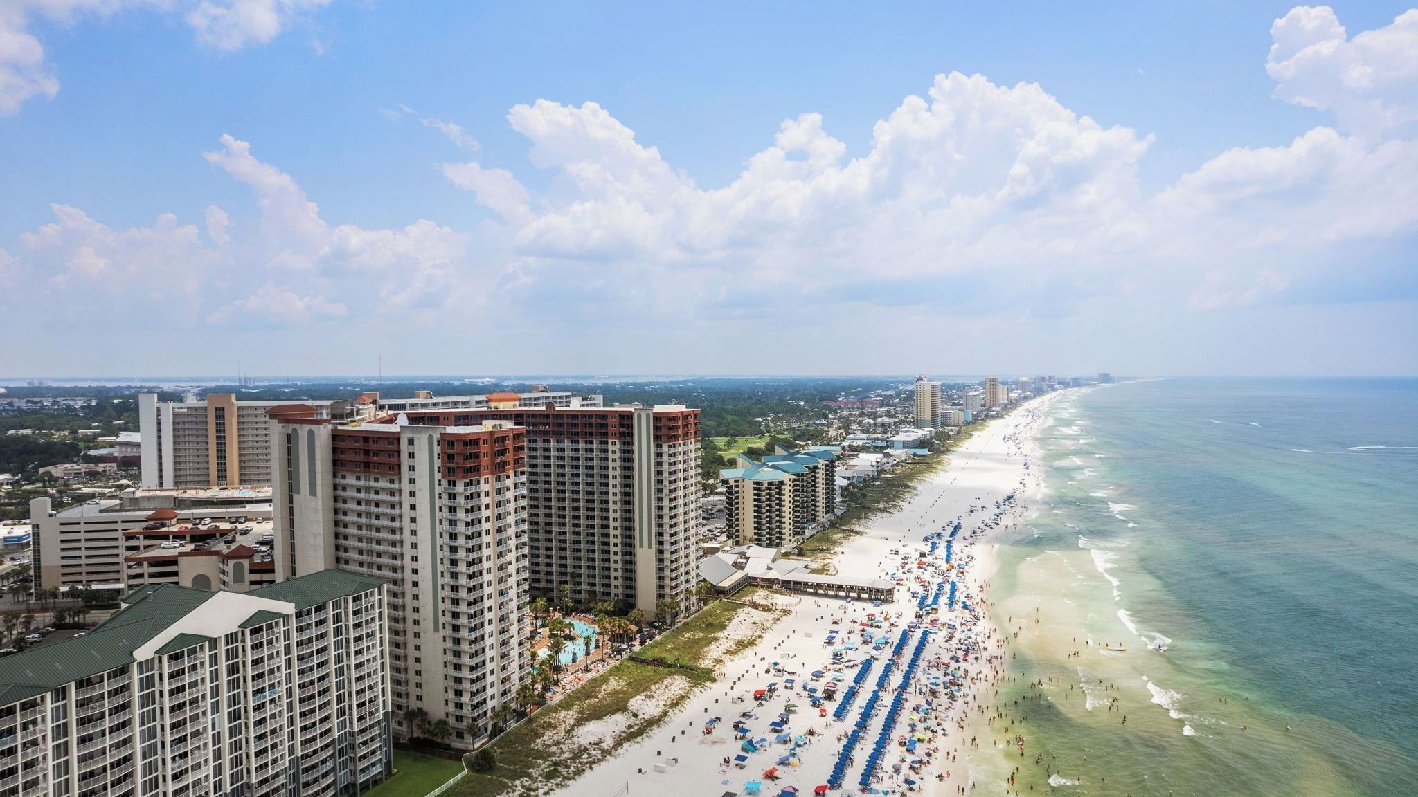A coastal cityscape with high-rise buildings, a beach with umbrellas, and a clear sky.