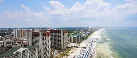 A coastal cityscape with high-rise buildings, a beach with umbrellas, and a clear sky.
