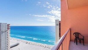Ein Balkon mit Blick auf Strand und Meer, ein Stuhl und ein Gebäude mit Balkonen.