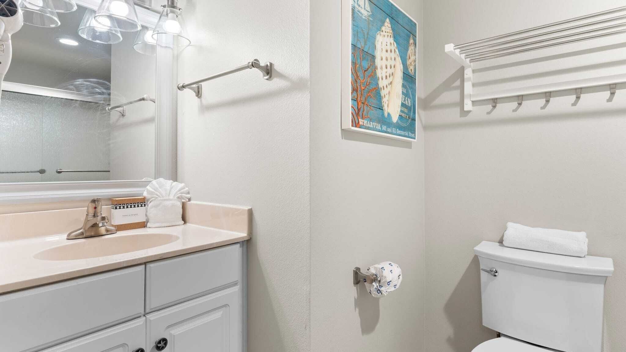 A bathroom with a sink, mirror, towel rack, toilet, and a framed picture on the wall.