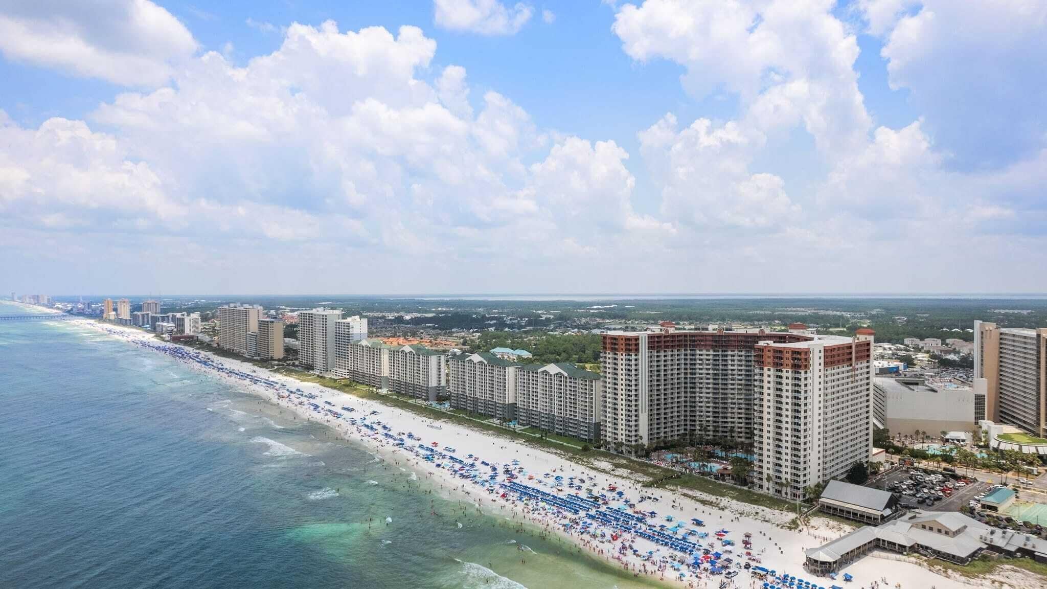 A coastal cityscape with a beachfront hotel featuring multiple high-rise buildings, a sandy beach, and a clear view of the ocean.