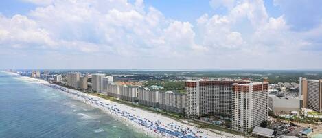 A coastal cityscape with a beachfront hotel featuring multiple high-rise buildings, a sandy beach, and a clear view of the ocean.