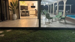 Un patio al aire libre con piscina, sillas verdes y una mesa de comedor.