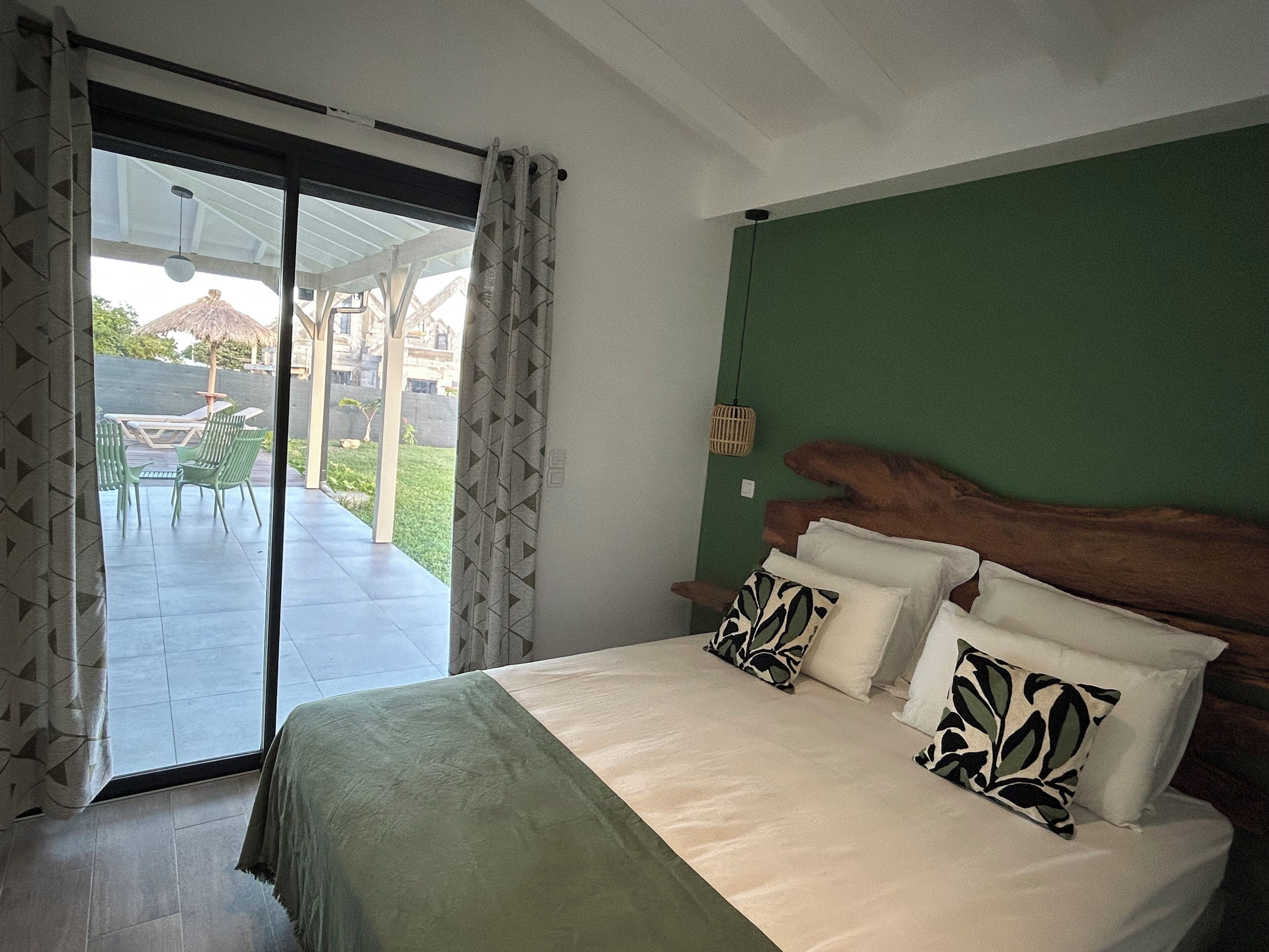 A bedroom with a large bed, green walls, and a view of an outdoor patio.