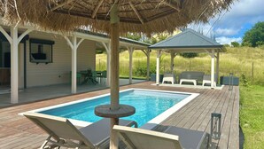 Un área de piscina con sillas de descanso y una zona de estar cubierta.