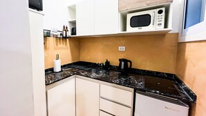 A compact kitchen with white cabinets, a black countertop, a microwave, and a dishwasher. - Rent Up - Estudio Moderno en Palermo (Buenos Aires)