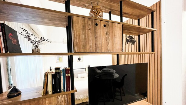 A modern living room with a wooden TV stand, a flat-screen TV, and a bookshelf. - Rent Up - Estudio Moderno en Palermo (Buenos Aires)