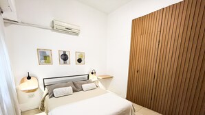 A bedroom with a bed, bedside lamps, an air conditioner, and a wooden panel wall. - Rent Up - Estudio Moderno en Palermo (Buenos Aires)