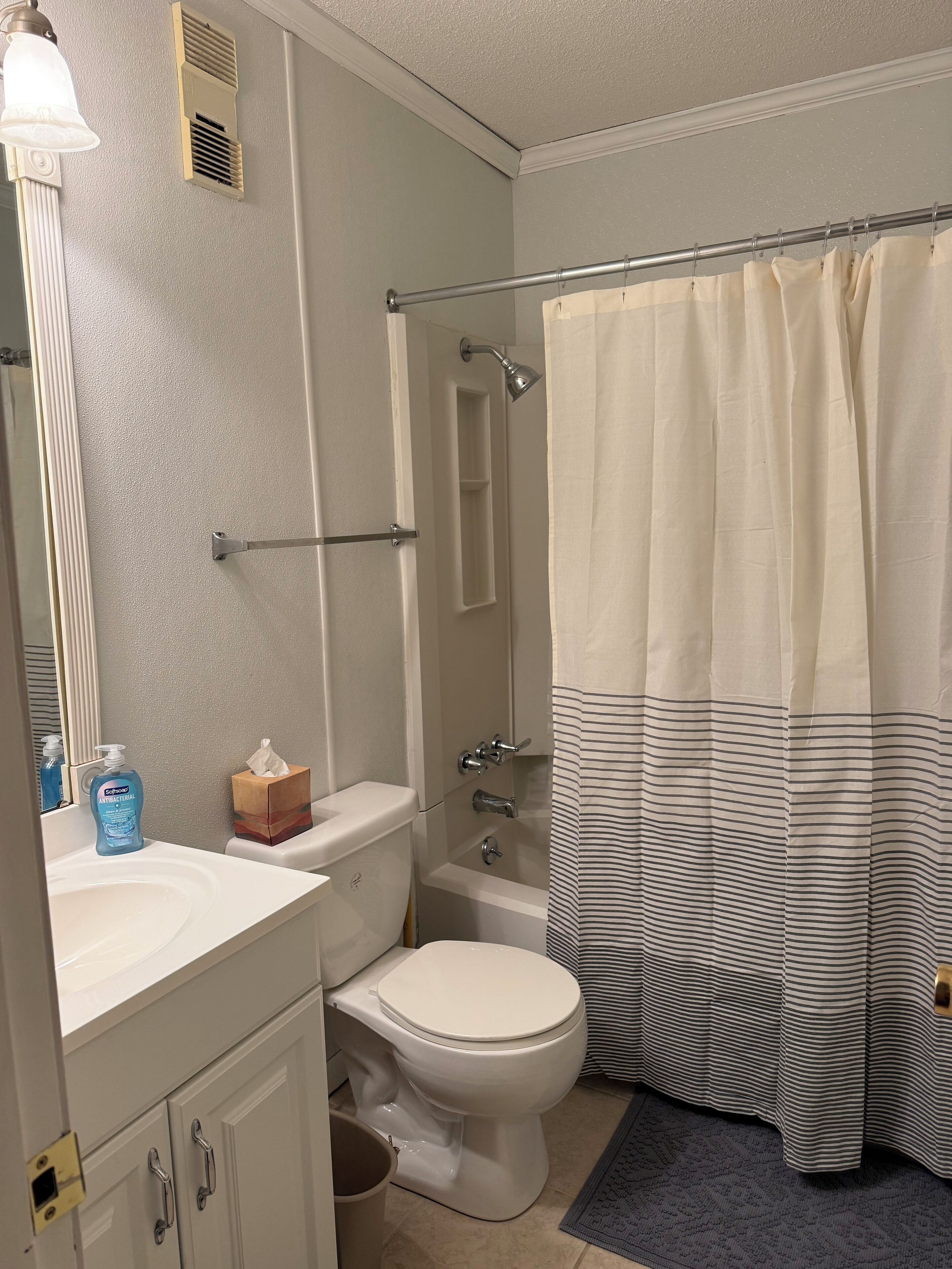 Un bagno con servizi igienici, lavabo, specchio, doccia e tenda da doccia a righe.