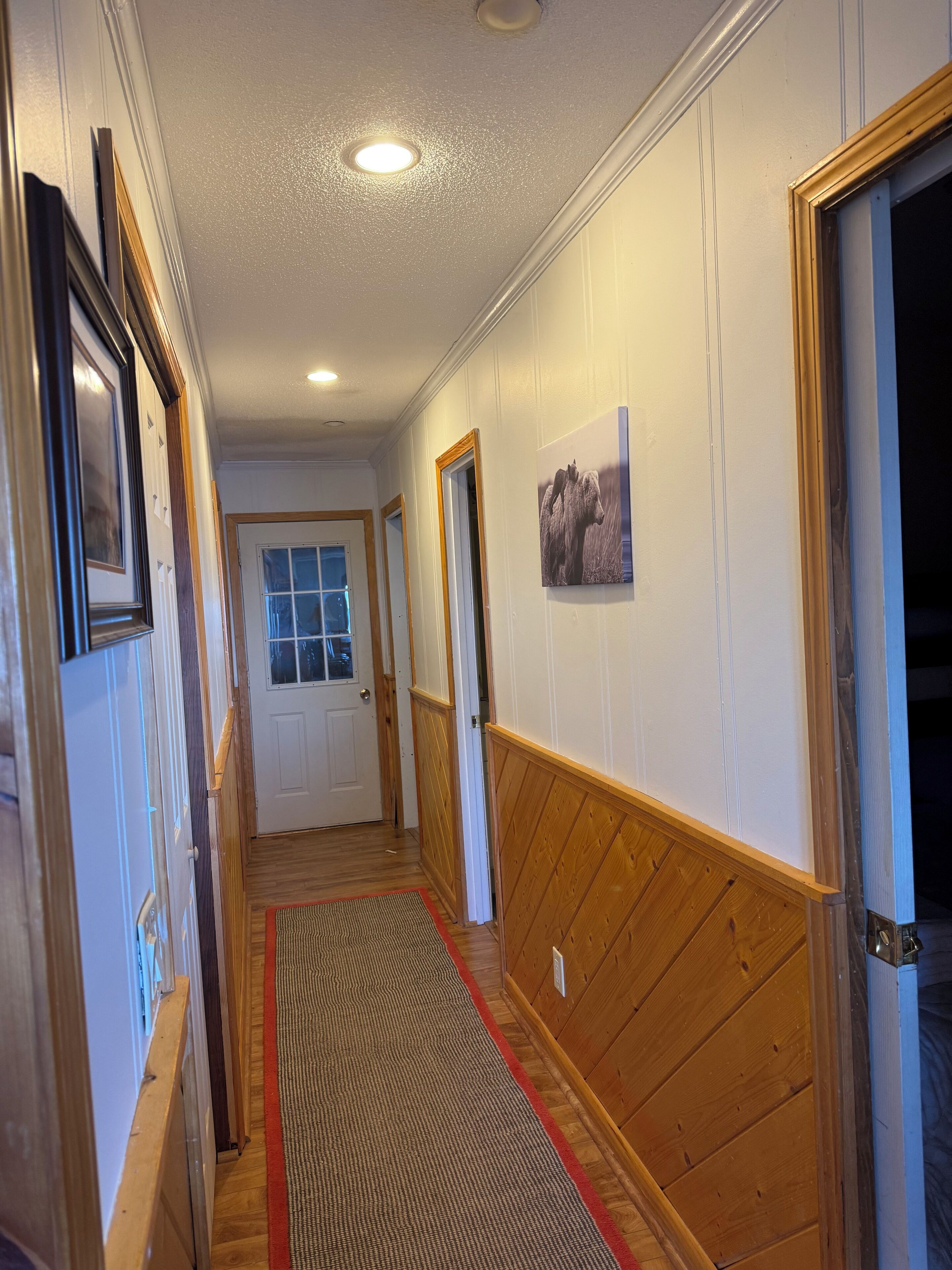 A hallway with wooden paneling, a red and beige rug, and a framed picture on the wall.