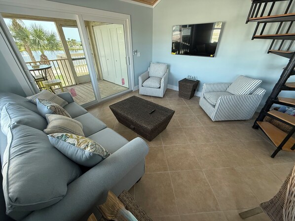 A living room with a grey sofa, striped armchairs, a woven coffee table, and a TV on the wall.