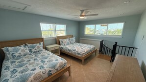 Ein Schlafzimmer mit zwei Betten, einem Nachttisch, einem Holzbüro, einem Deckenventilator und Fenstern mit Jalousien.