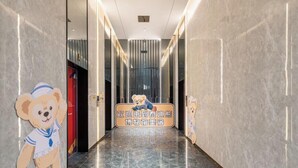 Un pasillo de hotel con paredes de mármol y suelo pulido. Se ve un oso como mascota en la pared izquierda.
