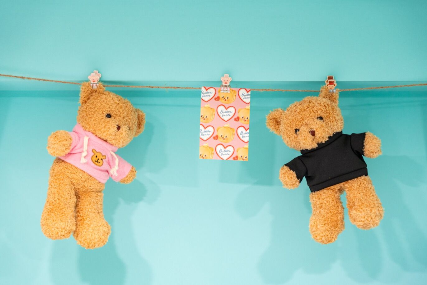 Dos ositos de peluche colgados en un tendedero sobre un fondo color turquesa.