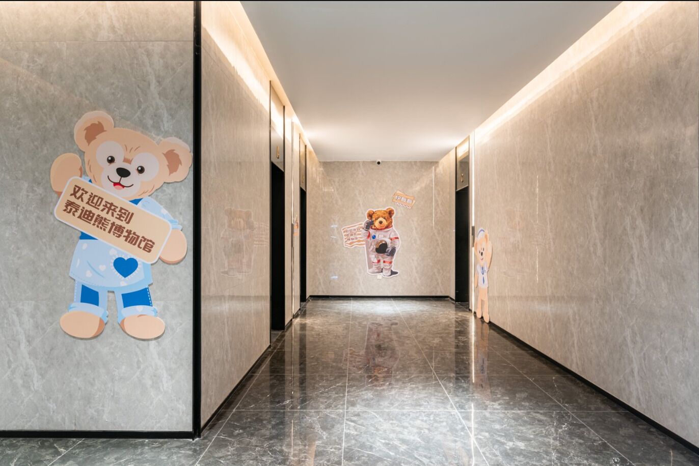 A hallway with marble walls and a polished floor, featuring cartoon bear decorations and a teddy bear in astronaut attire.