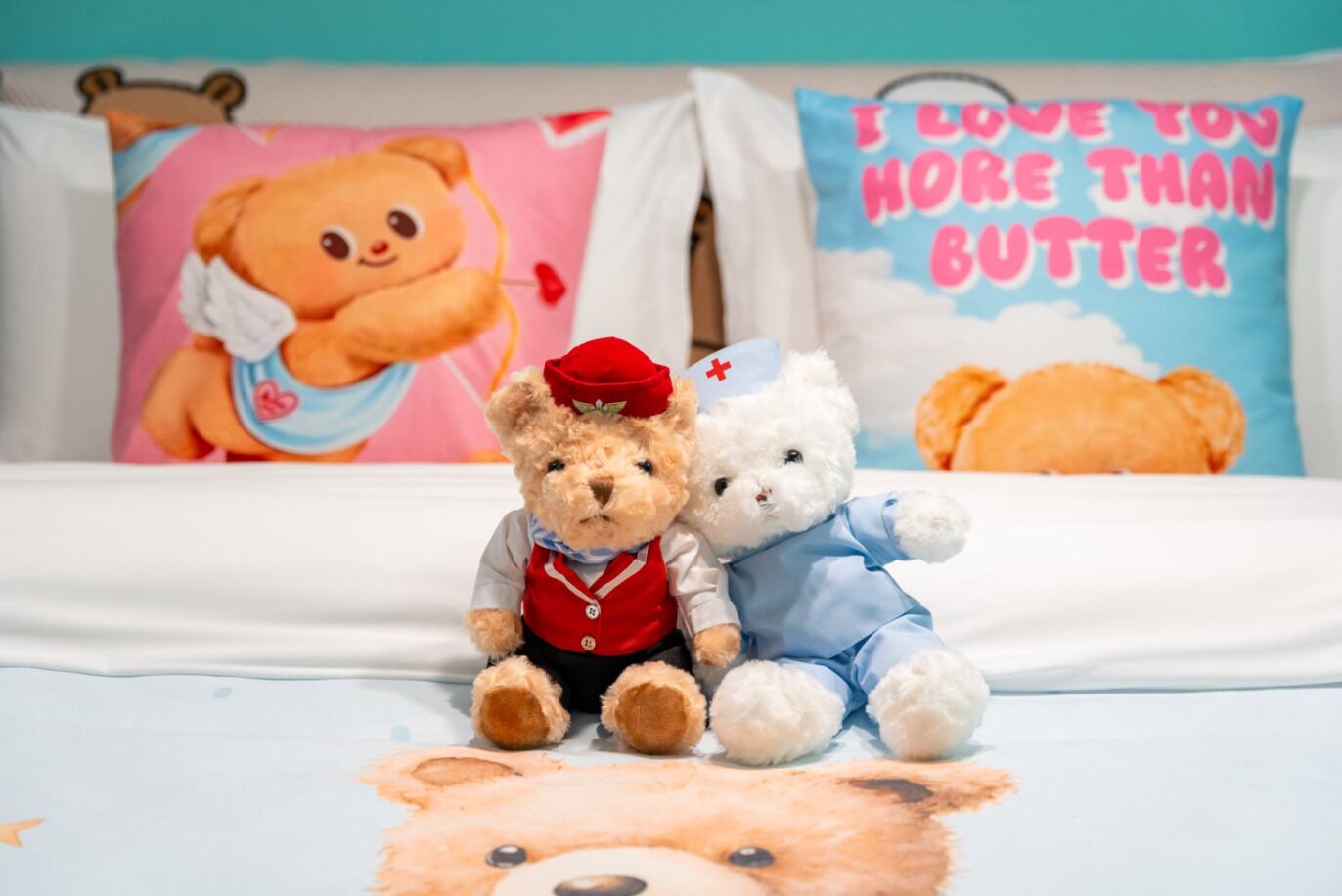 A bed with three teddy bears, two dressed as nurses and one as a bear, on a bed with a bear-themed bedspread.