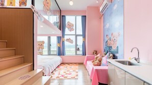 Habitación apta para niños con literas, una pequeña kitchenette y una ventana decorada con ositos de peluche.