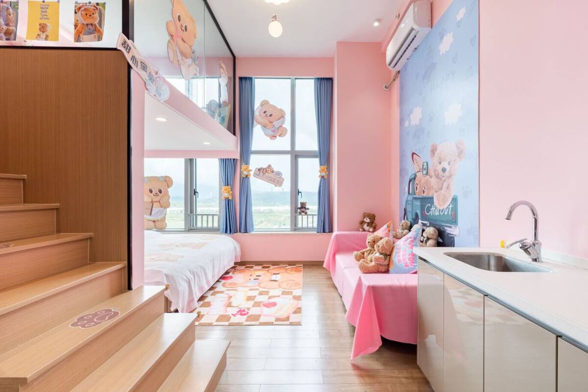 Une chambre conçue pour les enfants, avec un lit superposé, une petite kitchenette et une fenêtre décorée de motifs représentant des ours en peluche.