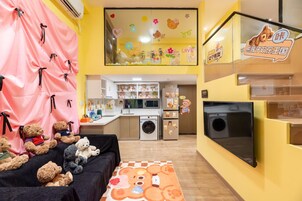 Una habitación acogedora con sofá, mesa y televisor. Hay ositos de peluche en el sofá y una zona de cocina al fondo.