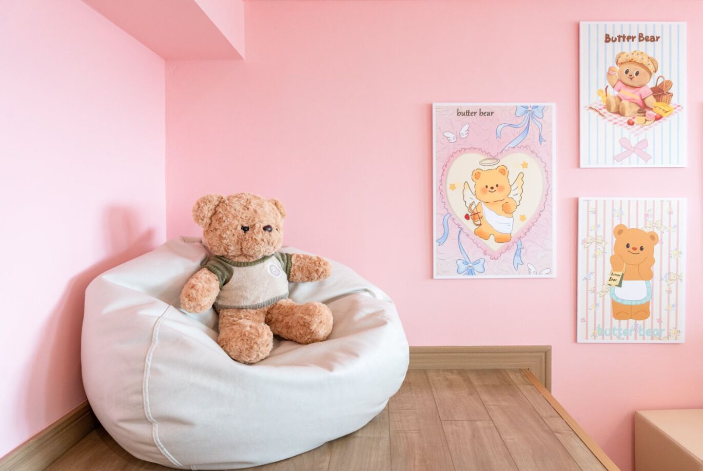 Um quarto com parede rosa, uma poltrona de tecido branco e três quadros na parede.