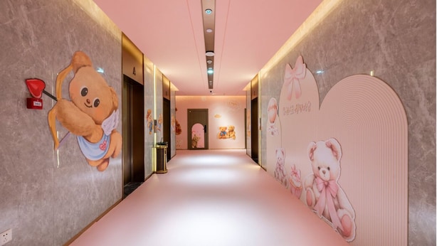 Un pasillo con alfombra rosa, adornos de ositos de peluche en las paredes y una puerta al final.