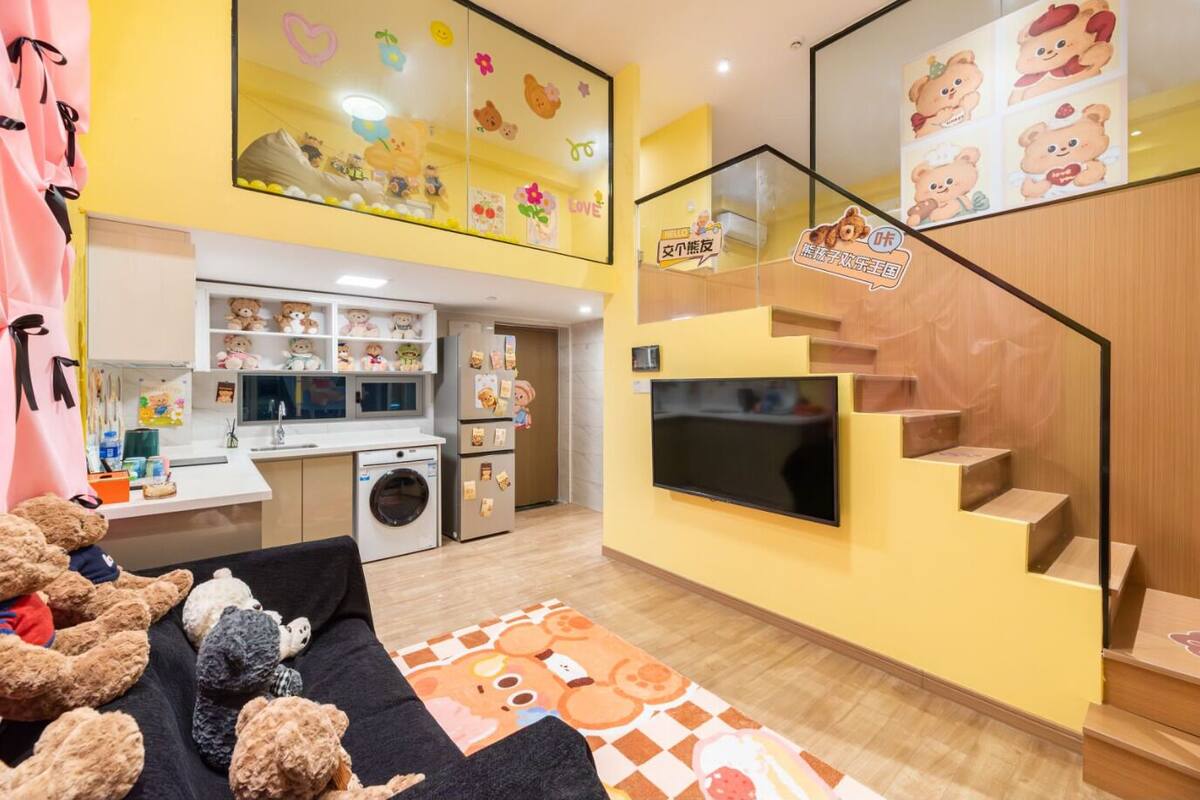 Un appartement moderne comprenant une cuisine, un espace de vie avec un canapé et des ours en peluche, une télévision et un escalier.