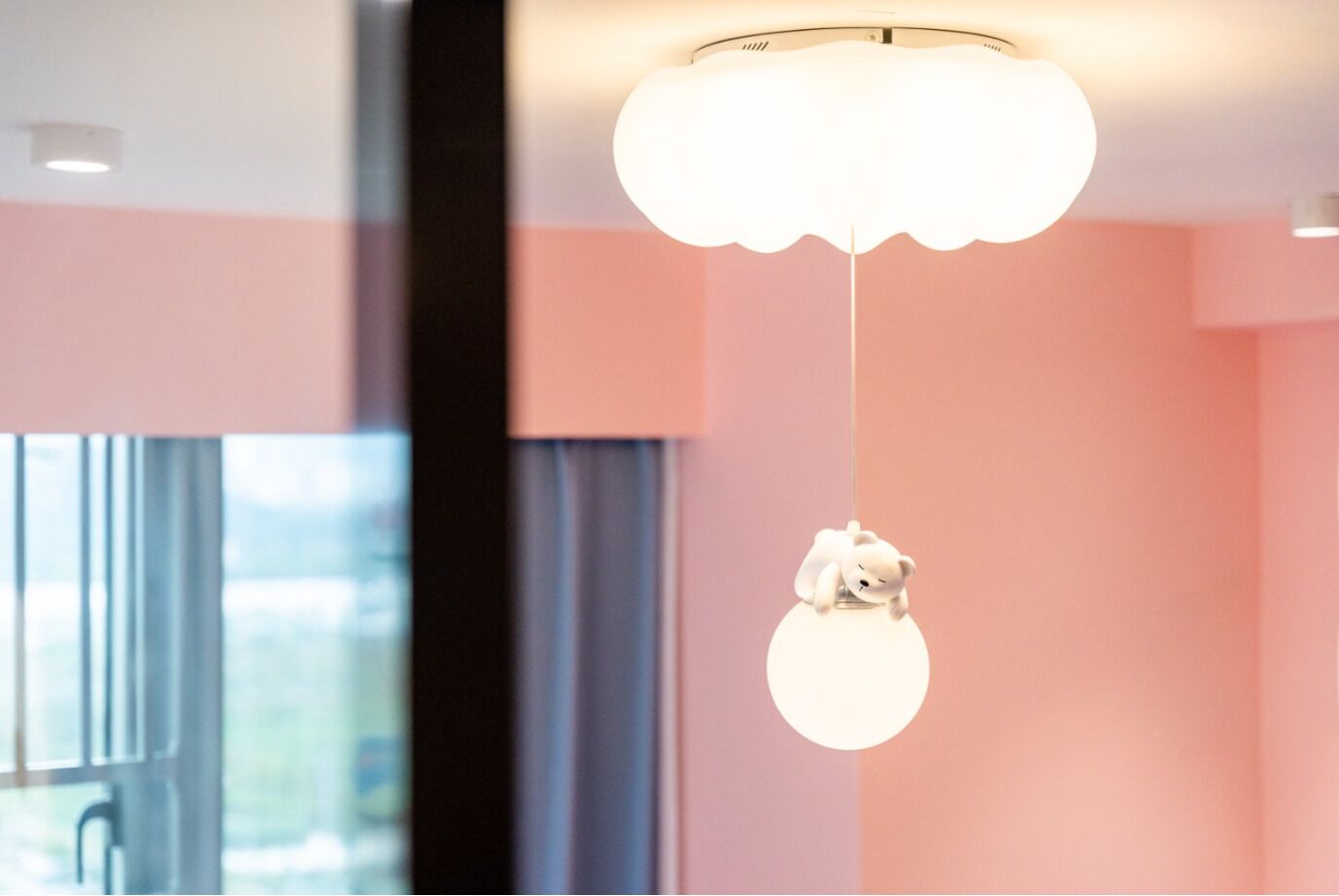 A modern interior with a large window, a white hanging light fixture, and pink walls.