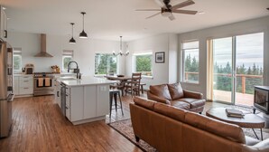 A spacious kitchen with a central island, a dining area with a table and chairs, a leather sofa, and a TV. - Misty Ridge (Homer)