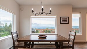 A dining room with a large window offering a view of a balcony and trees. - Misty Ridge (Homer)
