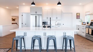 A modern kitchen with white cabinetry, a large island with bar stools, stainless steel appliances, and pendant lighting. - Misty Ridge (Homer)