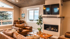 A living room with leather sofas, a fireplace, a TV, and a piano. - Little Bayview Cottage (Homer)
