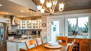 A modern kitchen with a central island, wooden chairs, and a dining table. - Little Bayview Cottage (Homer)