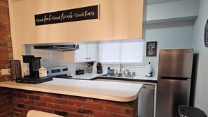 Een moderne keuken met een accentmuur van baksteen, een roestvrijstalen koelkast en een koffiezetapparaat op het aanrecht.