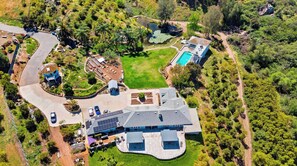 An aerial view of a large estate with a swimming pool, solar panels, and a winding driveway.