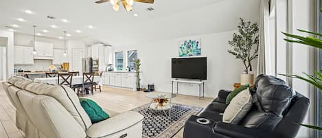 A modern living room with a sofa, a black leather couch, a ceiling fan, and a TV.